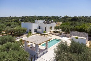 A modern house with a pool, surrounded by olive trees and a hilly landscape.