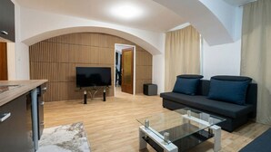 Ein modernes Wohnzimmer mit einer Couch, Fernseher, Glastisch und Wandpaneelen aus Holz.