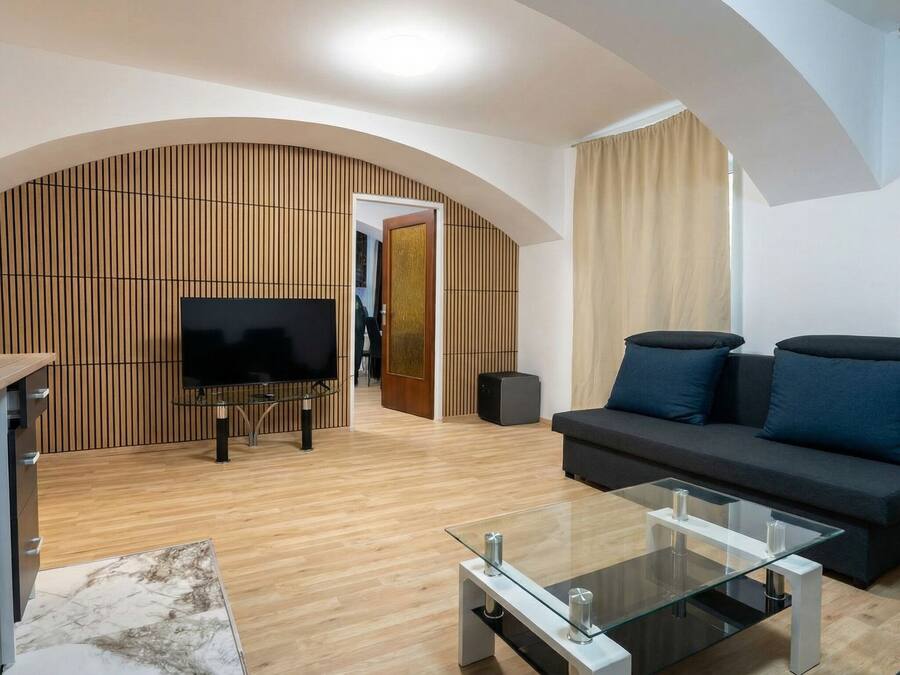 Una sala de estar moderna con sofá, televisor, mesa de centro de vidrio y pared de paneles de madera.