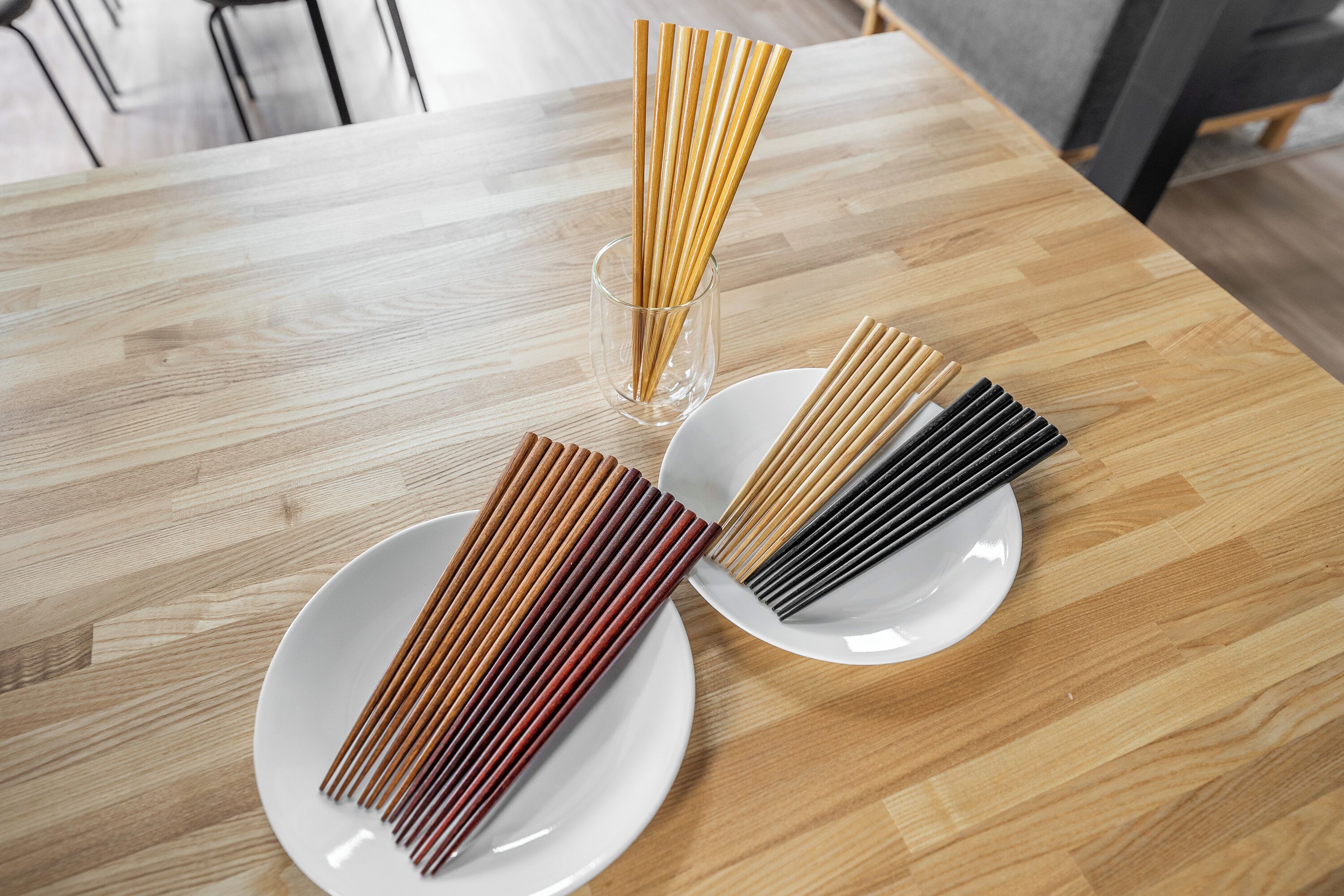 A wooden dining table with three white plates, each containing a set of chopsticks.