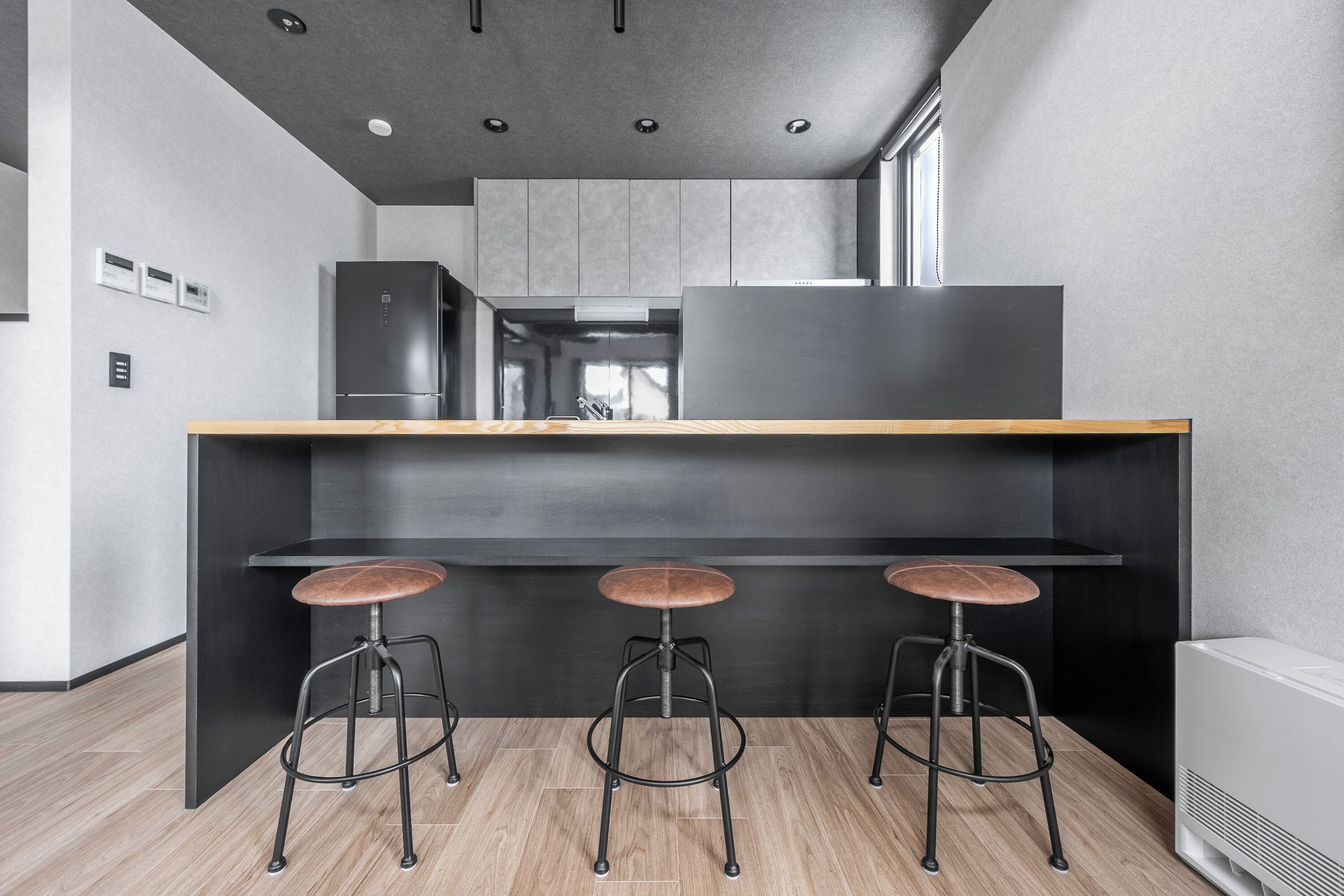 Una cocina moderna con una isla central, tres taburetes y un refrigerador empotrado.