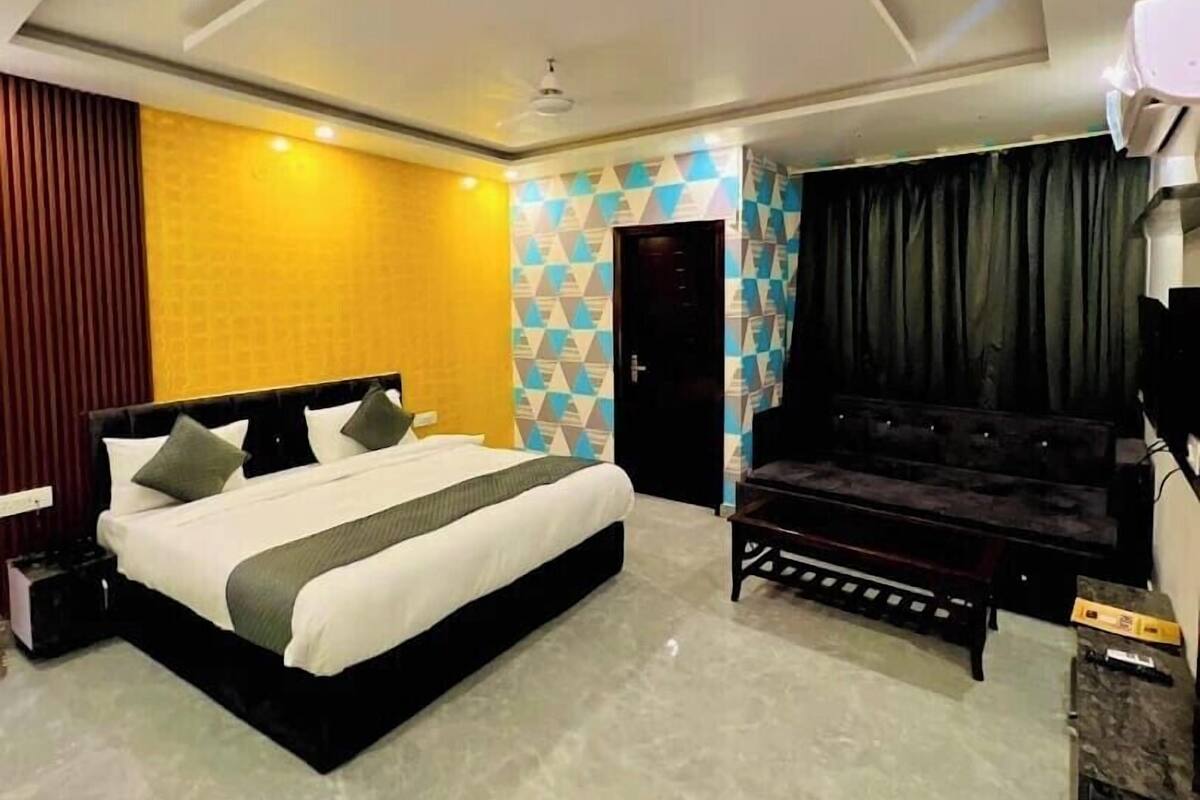 A modern hotel room with a large bed, a sofa, a ceiling fan, and a built-in air conditioning unit.