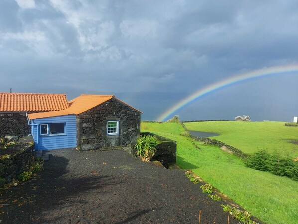 A rural landscape with a stone house, a blue door, and a rainbow.