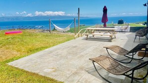 A patio with a view of the ocean, a hammock, and outdoor furniture. - Modern and cozy house in Ribeirinha, Pico Island (Ribeirinha)