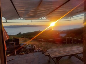 A patio with a wooden table and a metal railing overlooking a body of water during sunset.