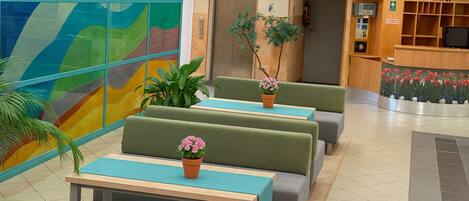 Un vestíbulo de hotel con asientos verdes, un mostrador de recepción y un mural de pared colorido.