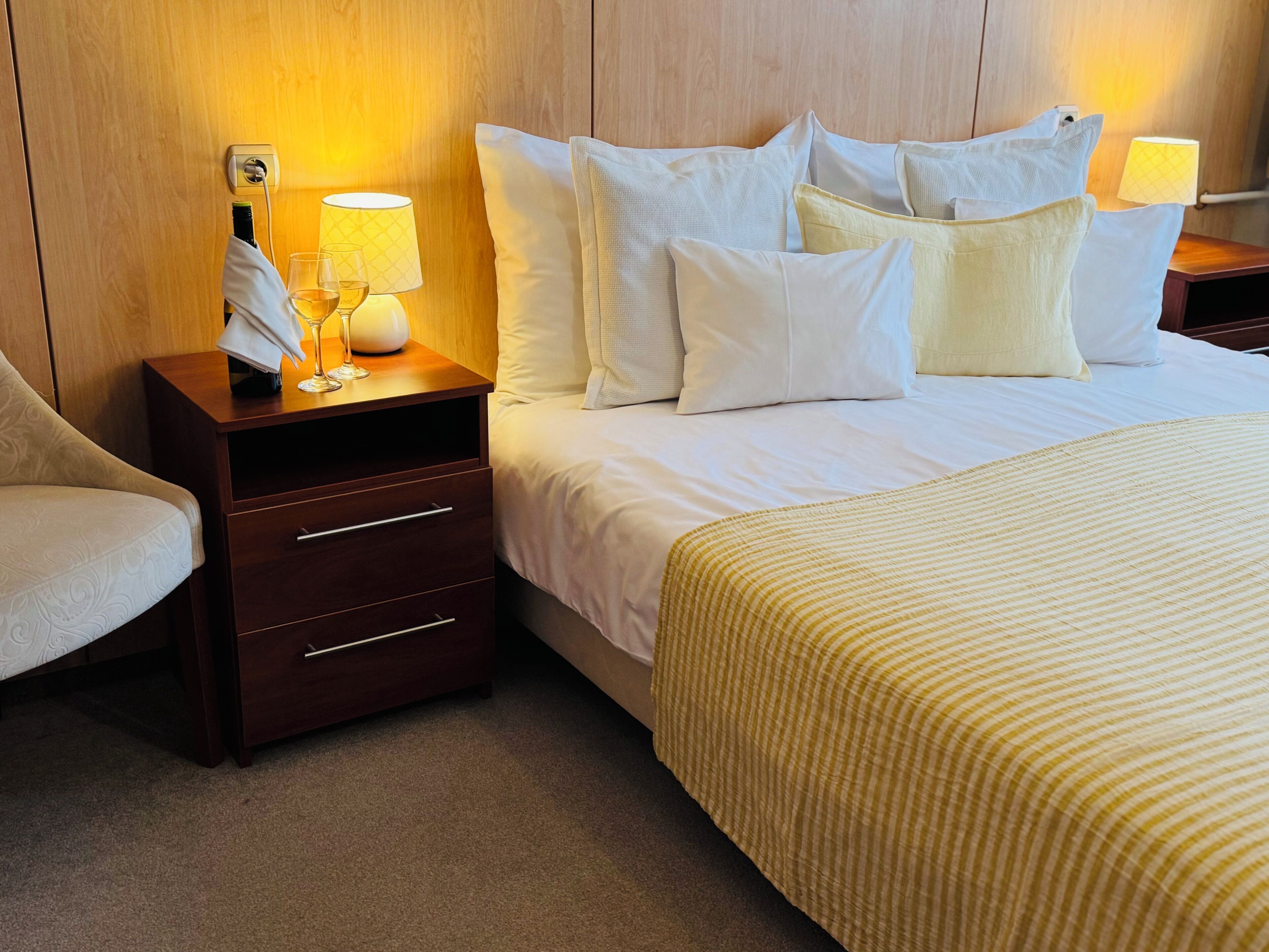Habitación de hotel con cama, mesita de noche, lámpara, teléfono y silla.