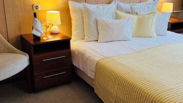Habitación de hotel con cama, mesita de noche, lámpara, teléfono y silla.