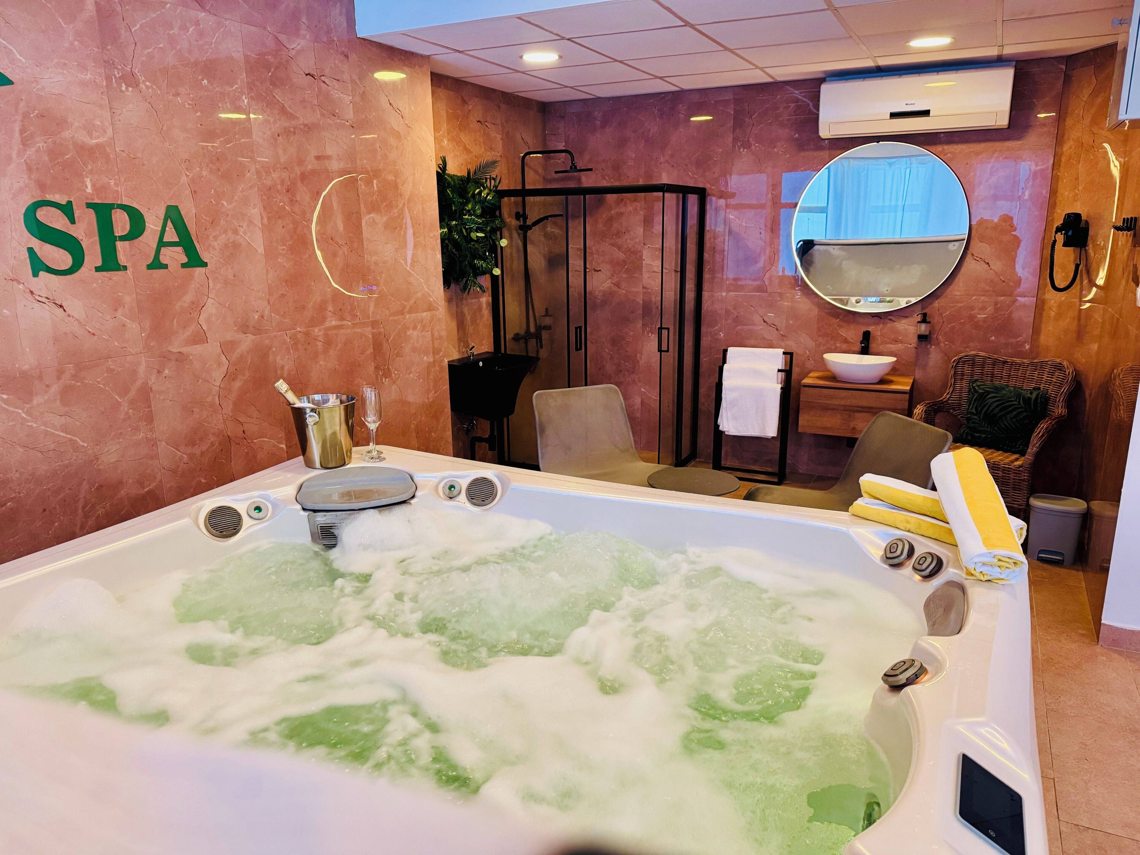 A spa room with a large bathtub filled with bubbles, a sink, a mirror, and a wicker chair.