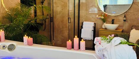 A bathroom with a bathtub, candles, a shower, a sink, and a mirror.