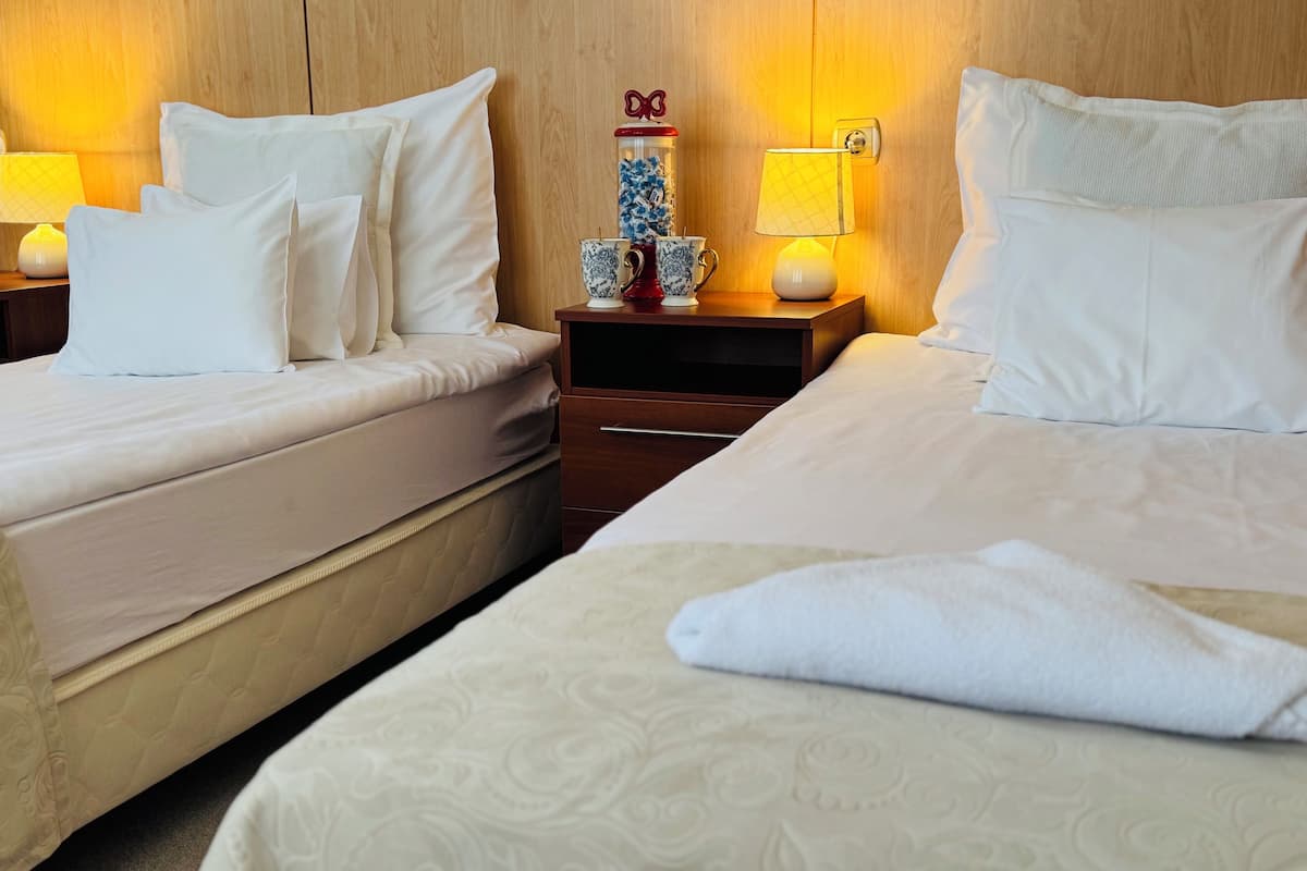 A hotel room with two beds, a nightstand with a lamp, a decorative vase, and a wooden headboard.