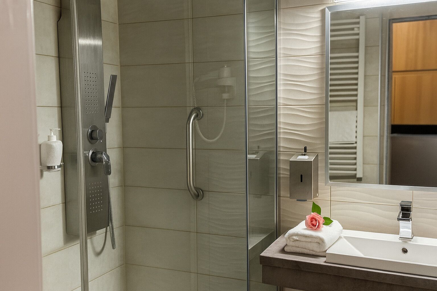 Une salle de bain moderne avec une douche à parois de verre, un lavabo intégré et une serviette ornée d’une rose posée sur le comptoir.