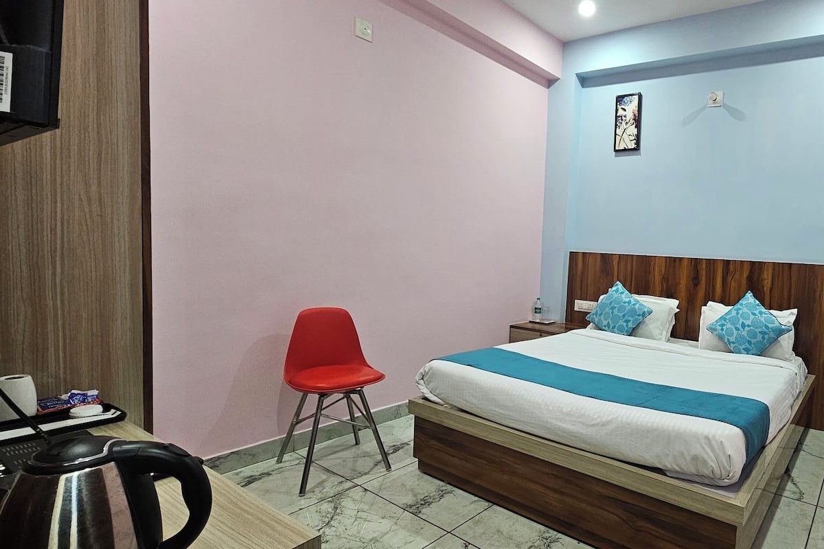 Une chambre à coucher avec un lit, une chaise rouge, une tête de lit en bois et une petite table sur laquelle se trouvent un clavier et une souris.