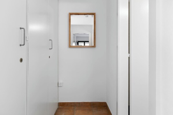 Een smalle gang met witte muren, een spiegel met houten lijst aan de wand, en een betegelde vloer.