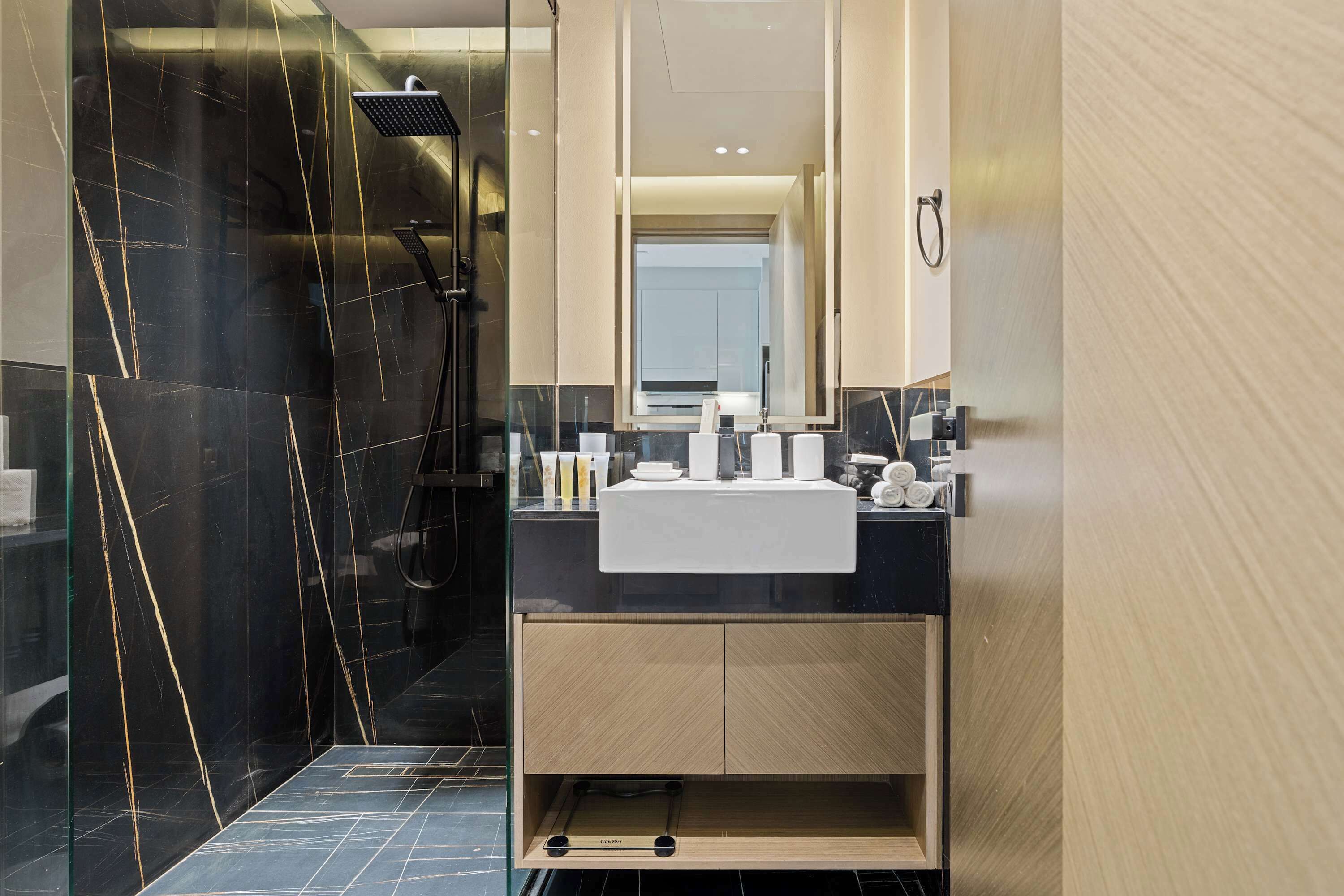 A modern bathroom with a black marble shower, a white sink, and a wooden vanity.