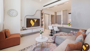 Een moderne woonkamer met een bank, een salontafel en een aan de muur bevestigde televisie. Achtergrond toont een eethoek met een tafel en stoelen.