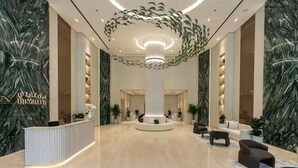 Een ruime lobby met een centrale kolom, een receptiebalie en een modern plafondontwerp.