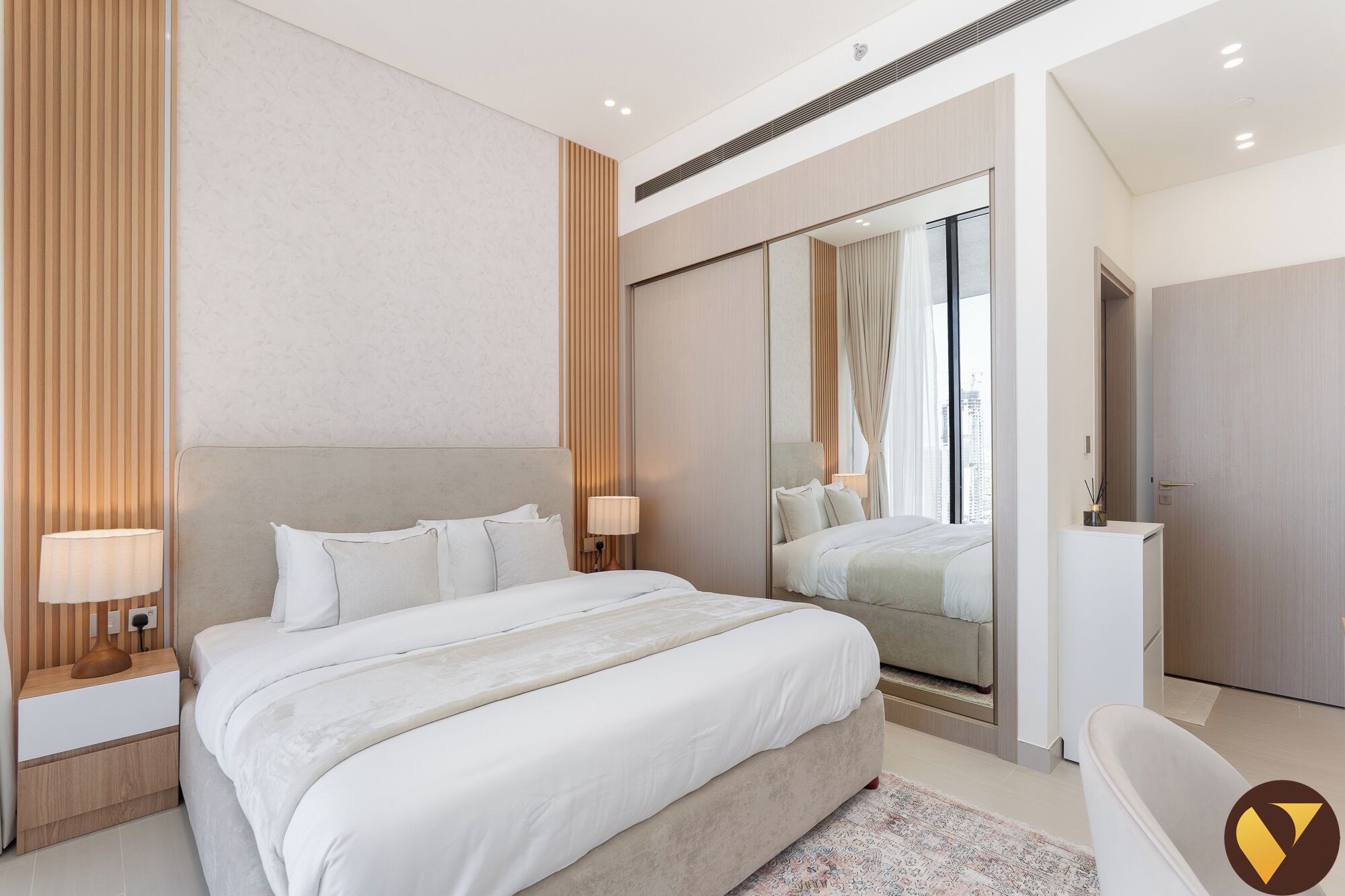A modern hotel room with a large bed, bedside lamps, a mirror, and a view of the city.