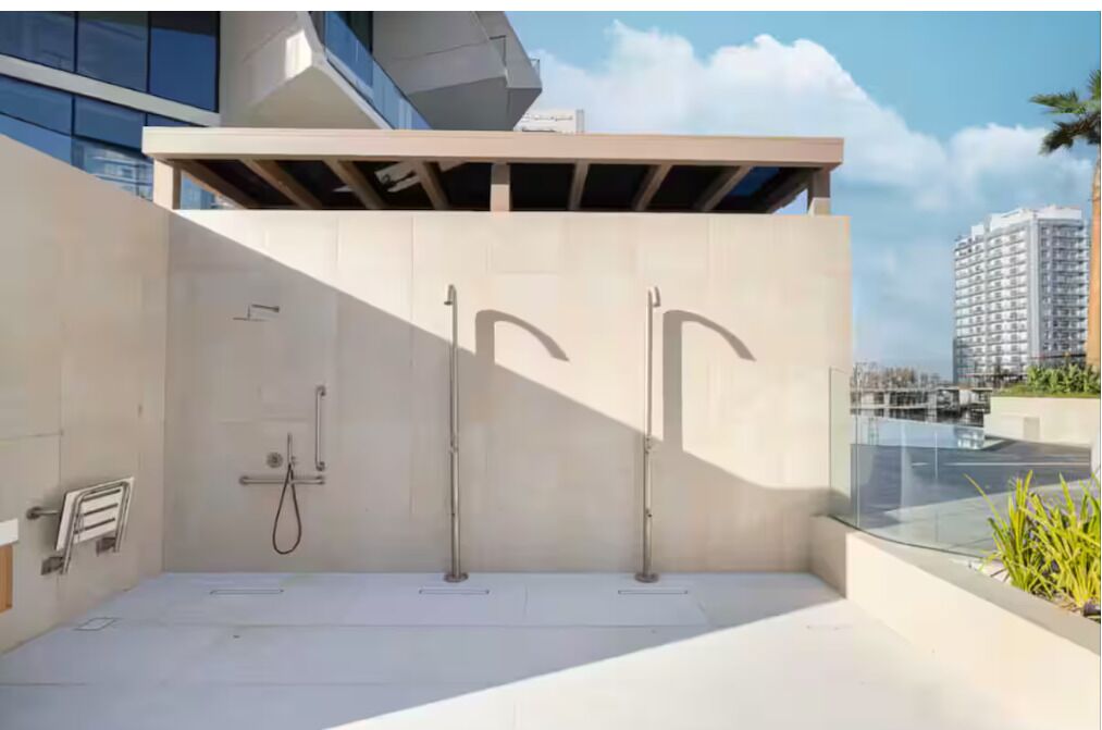 A modern outdoor shower area with two showerheads, a towel rack, and a glass railing overlooking a cityscape.