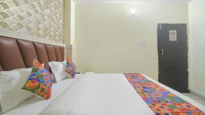 A hotel room with a bed, pillows, a headboard, a door, and a wall with a textured pattern. - Hotel Magadh Crystal (Patna)