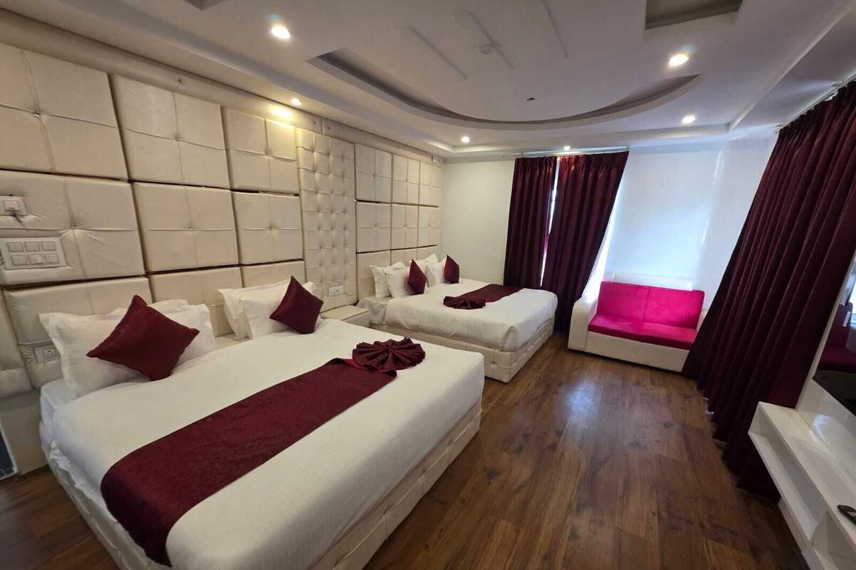 A hotel room with two beds, a sofa, a large padded headboard, and a wooden floor.
