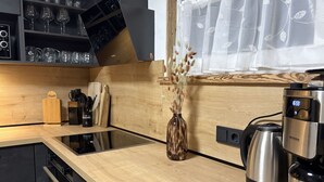 Una cocina moderna con encimera de madera, horno empotrado, cafetera y un florero con plantas secas.