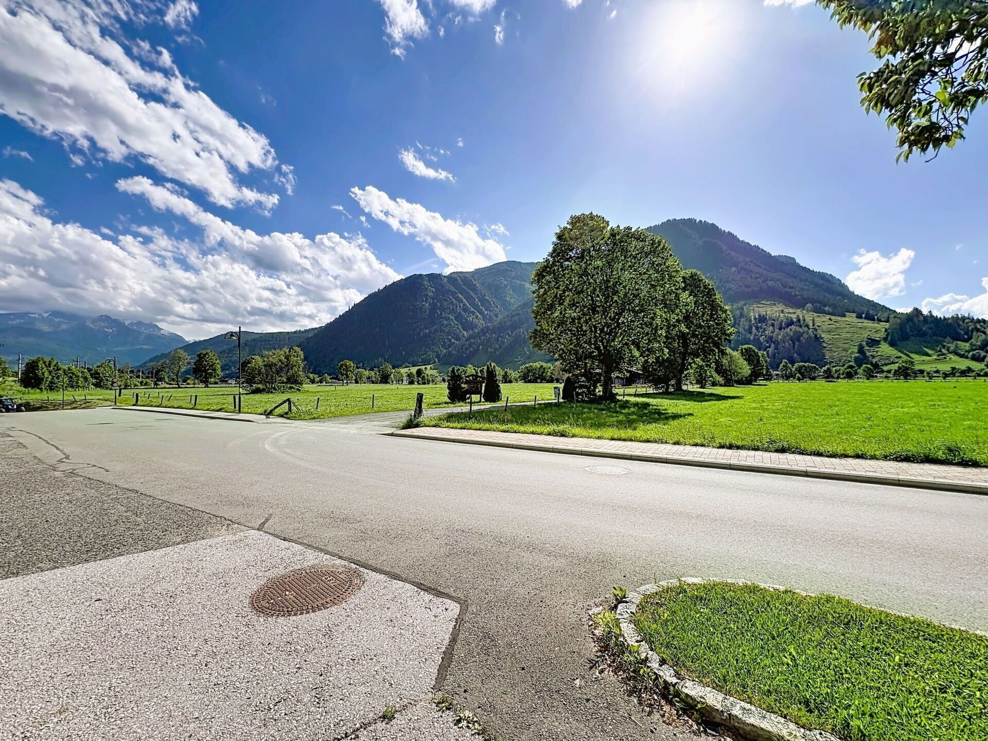 Eine ländliche Straße mit Kreisverkehr, einem großen Baum und einem Berg im Hintergrund.