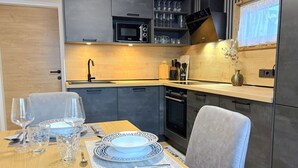 Una cocina moderna con armarios oscuros, un microondas y un lavabo. Hay una mesa de comedor puesta con platos, vasos y una vela.
