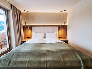 Una habitación de hotel moderna con una cama grande, dos mesitas de noche y vistas al exterior a través de un amplio ventanal.