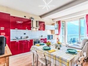 Eine moderne Küche mit roten Schränken, ein Essbereich mit Tisch für zwei Personen und ein Balkon mit Blick.
