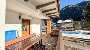 Un banco de madera frente a un edificio con piso de piedra, una puerta y una vista de la montaña al fondo.