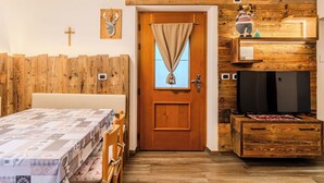Una habitación acogedora con una pared de madera, una cama con colcha estampada, una puerta de madera con cortina, un televisor y un pequeño armario de madera.