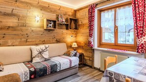 Una habitación acogedora con una pared de madera, un sofá con mantas estampadas, una mesa con mantel y una ventana con cortinas.