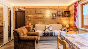 Una habitación acogedora con una pared de madera, un sofá, un sillón marrón, una mesa de madera y una ventana con cortinas.