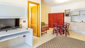 Un espace de vie compact comprenant un téléviseur, une table à manger avec des chaises, un coin cuisine avec un four à micro-ondes et une armoire.