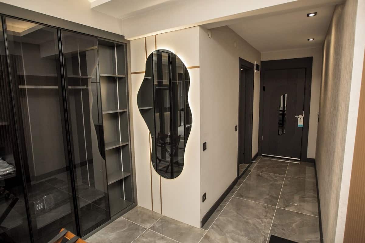 Un pasillo con un mueble de almacenaje de vidrio, un espejo curvo y una puerta que da a otra habitación.