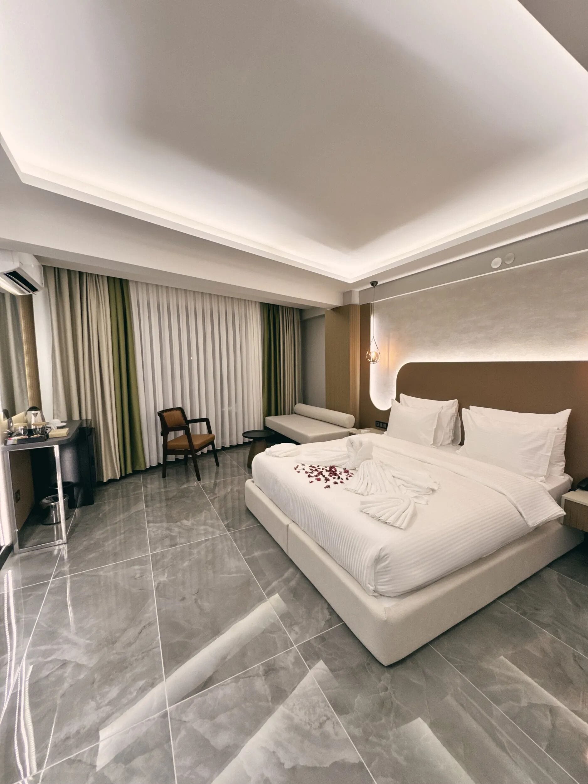 A modern hotel room with a large bed, a desk, a chair, and a sofa.