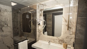 Ein modernes Badezimmer mit einer gläsernen Dusche, einem Marmor-Waschtisch und einem großen Spiegel.