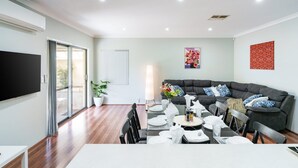 Un salon moderne avec un canapé d’angle gris, une table à manger pour quatre personnes et un grand téléviseur à écran plat fixé au mur.