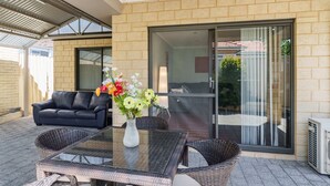 Un espace patio extérieur avec une table et des chaises en verre, un canapé en cuir noir et un vase rempli de fleurs.