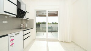 Una cocina moderna con lavavajillas integrado, cafetera y un amplio ventanal corredera que da a un balcón.