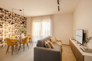 A modern living room with a sofa, dining table, and chairs. There is a television on a stand and a plant on the table. - Urban Penthouse Terrace with Parking (Bari)
