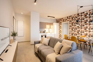 A modern living room with a sofa, a dining area with chairs, a kitchen in the background, and a patterned wall. - Urban penthouse with a terrace and parking space (Bari)