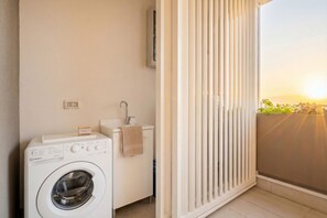 A laundry room with a washing machine, a sink, and a window with blinds. - Urban Penthouse Terrace with Parking (Bari)