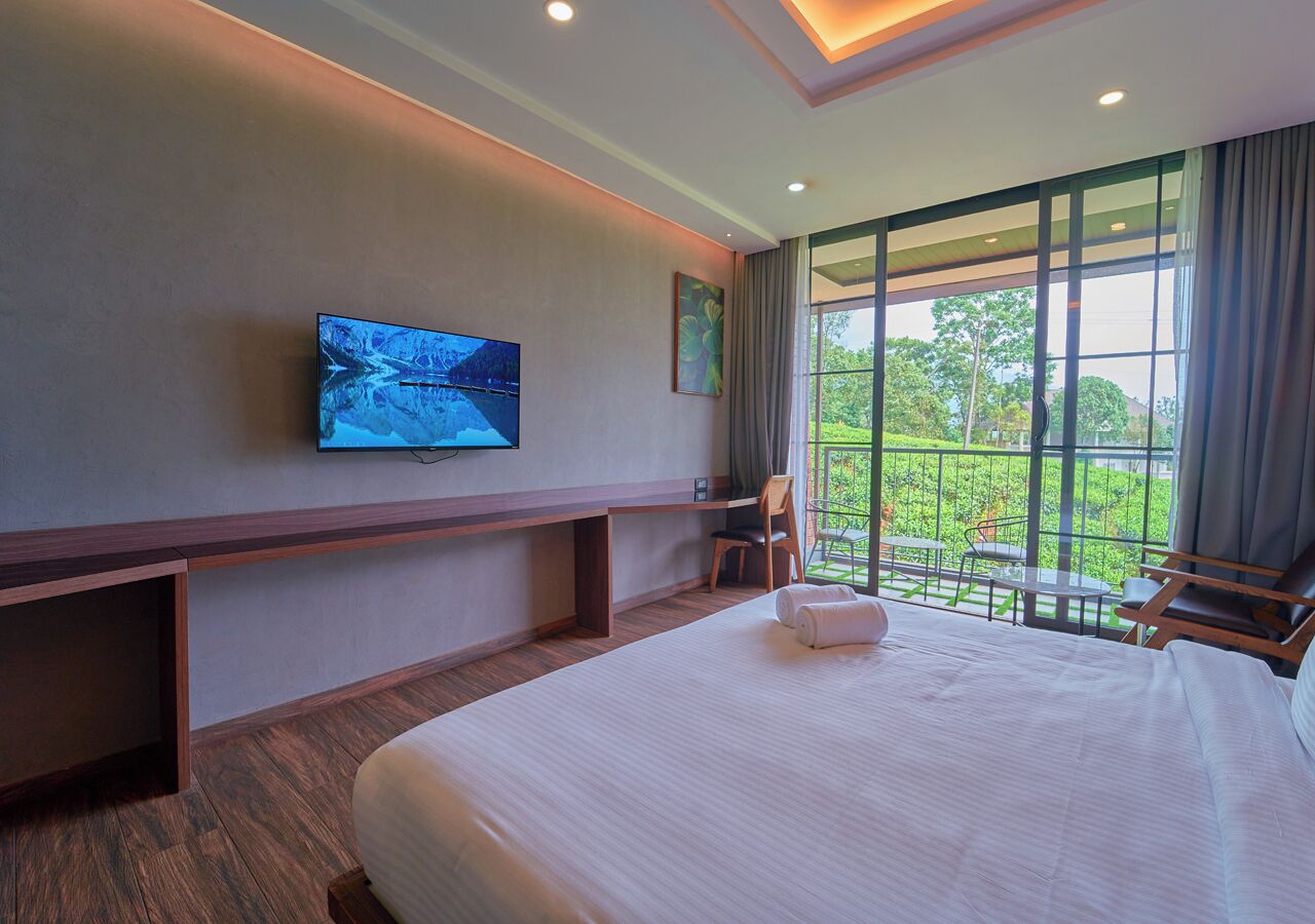 Habitación de hotel con una cama grande, televisión montada en la pared, escritorio y balcón con mobiliario exterior.