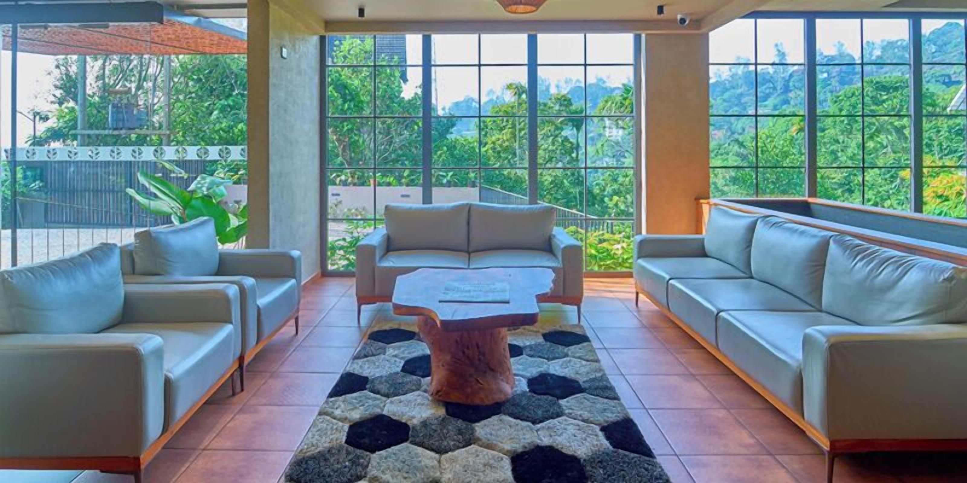 A spacious living area with a sofa set, a coffee table, and a view of lush greenery through large windows.