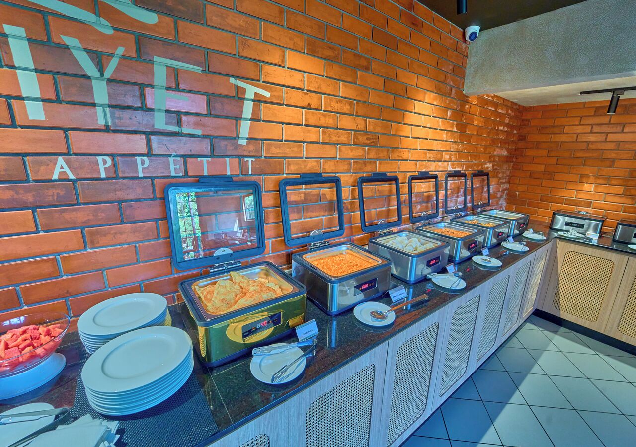 A buffet setup with various food items and plates, a brick wall with the word "APPETIT" visible, and a security camera.