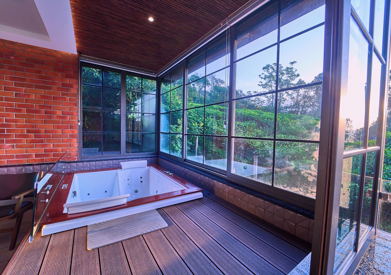 A modern bathroom with a large bathtub, wooden flooring, and large windows offering a view of greenery.