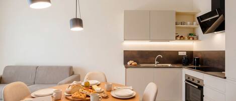 A modern kitchen with a dining area, including a table set for two with plates, cups, and a basket of bread.
