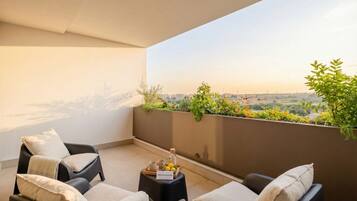 A balcony with two black lounge chairs, a small table with a tray of lemons, and a view of a cityscape.